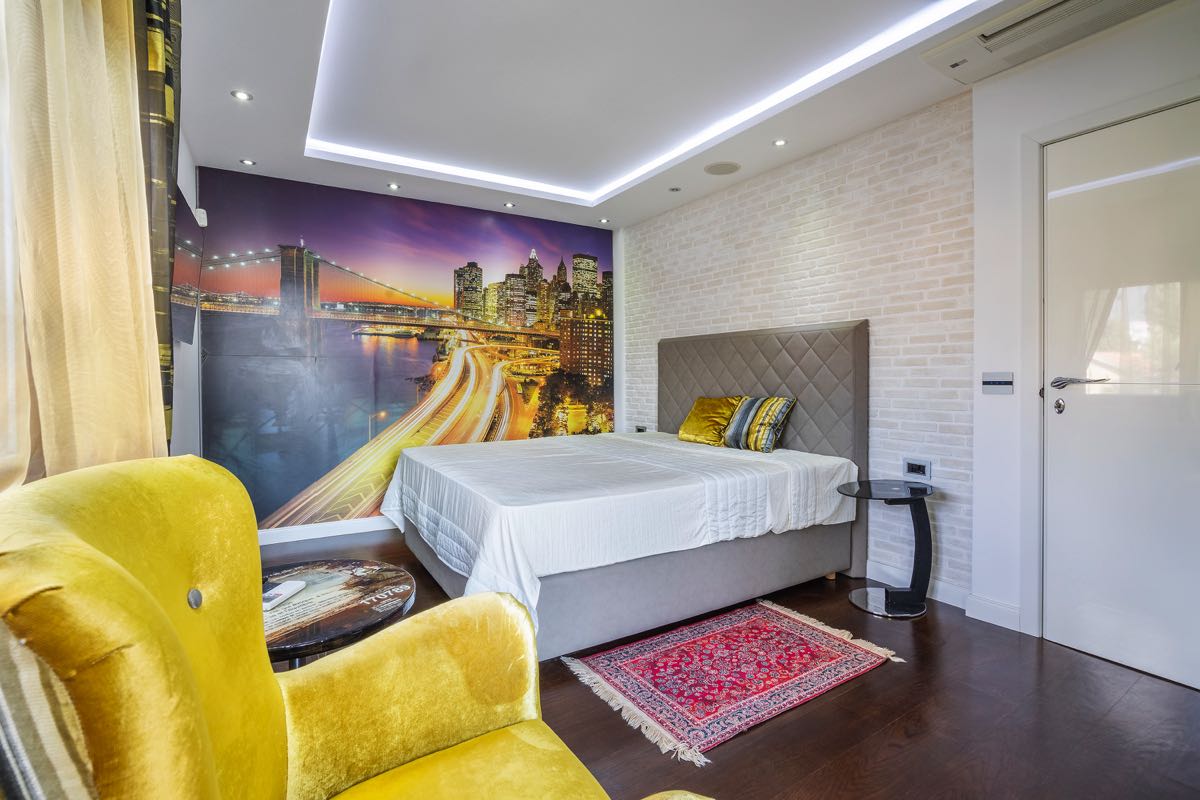 Modern bedroom in a villa in Budva, Montenegro: double bed, city mural, yellow armchair, and decor.