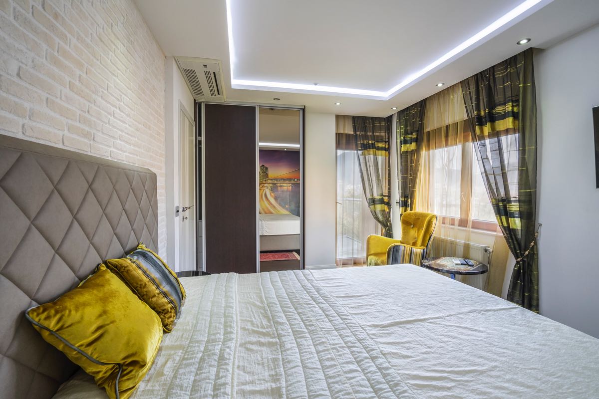Modern bedroom in a villa in Budva, Montenegro: double bed, brick wall, built-in wardrobe, and a yellow armchair.