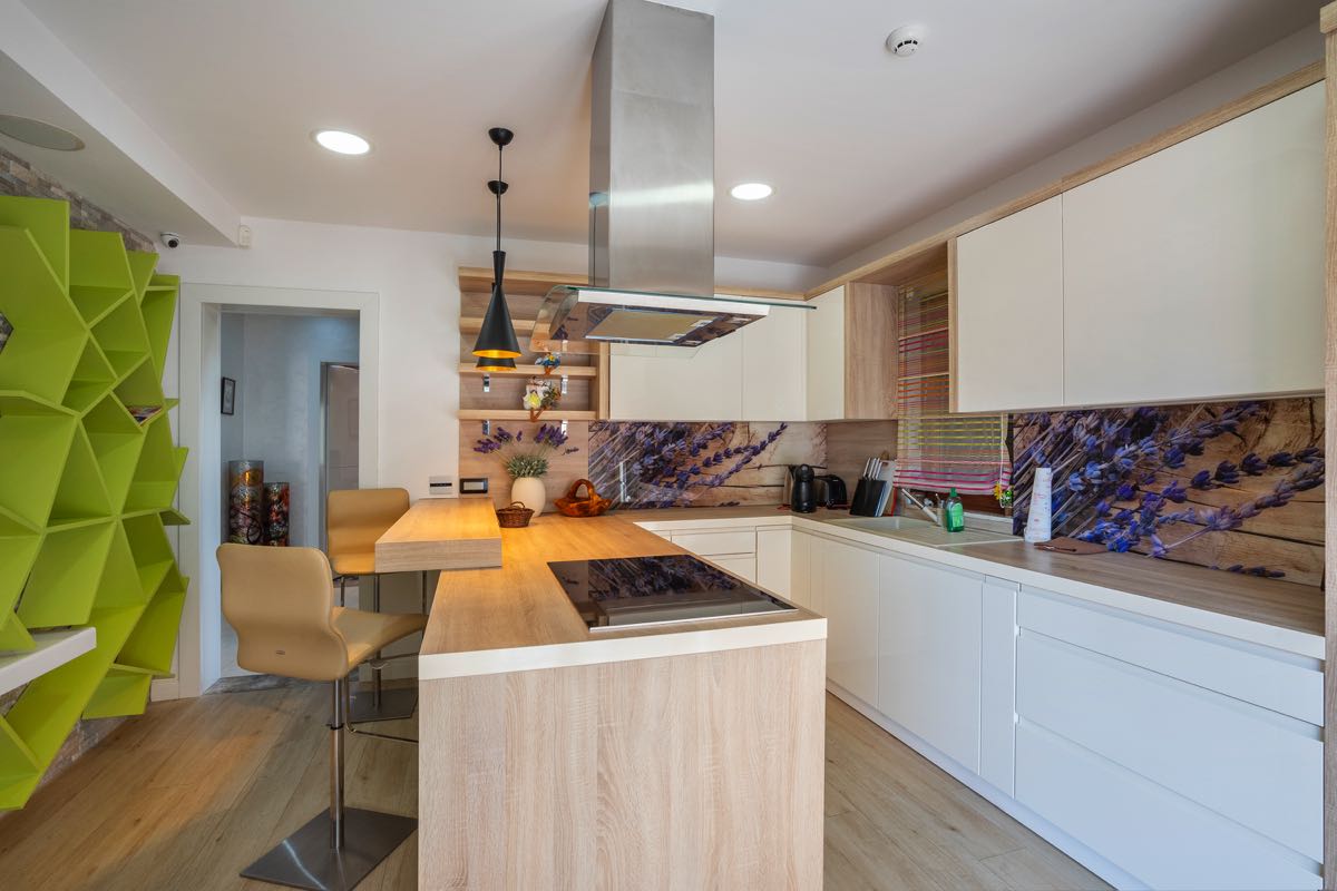 Modern kitchen in a villa in Budva, Montenegro: light cabinetry, a breakfast bar, a lavender backsplash, and a bright shelving unit.