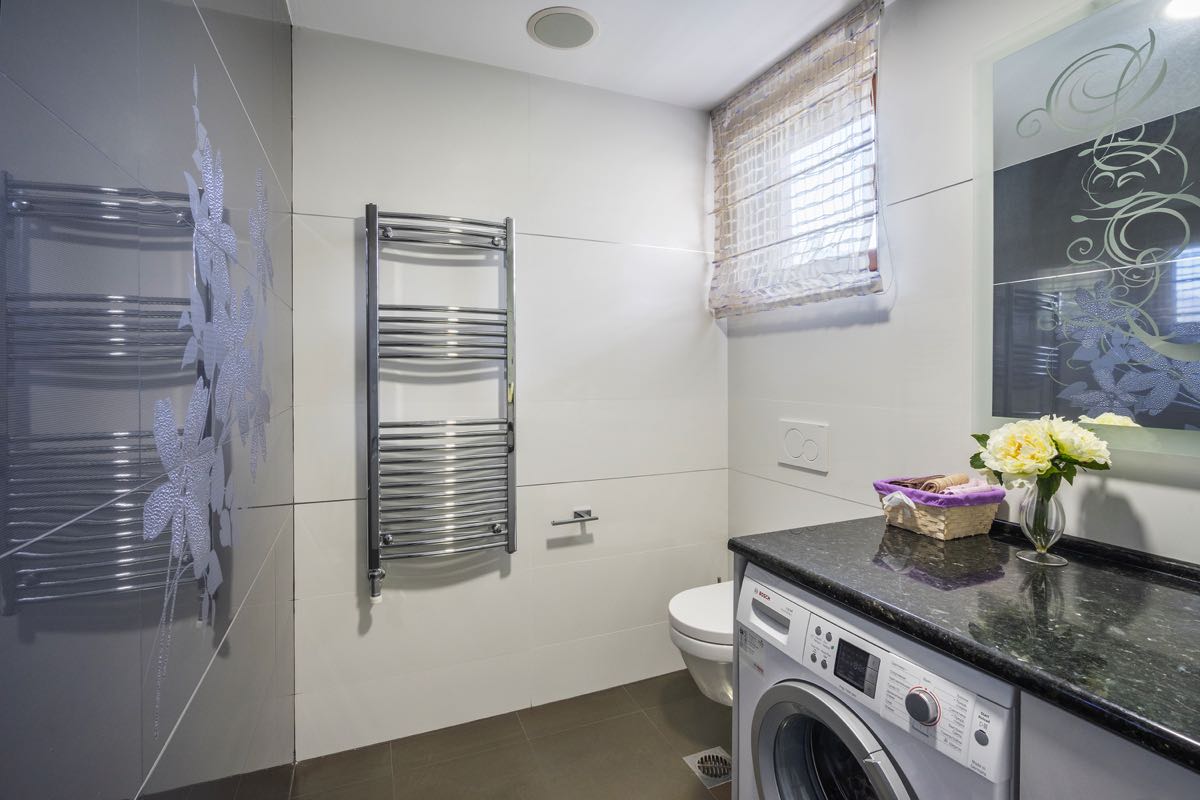 Modern bathroom in a villa in Budva, Montenegro: stylish finishes, washing machine, and a mirror with decor.