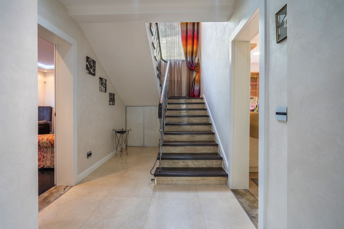 Villa interior in Budva, Montenegro: a bright hall with a dark wood staircase and wrought-iron railings.