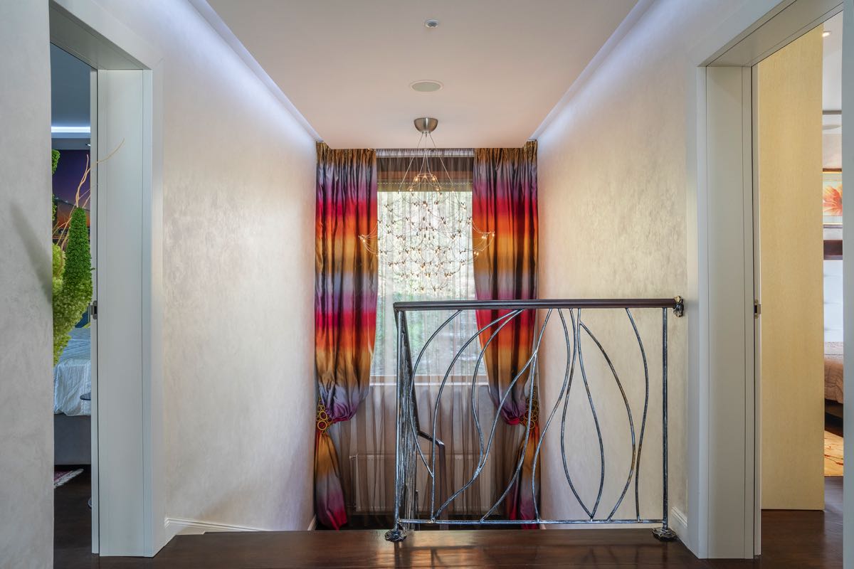 Villa interior in Budva, Montenegro: staircase hall with designer curtains, wrought-iron railings, and a chandelier.