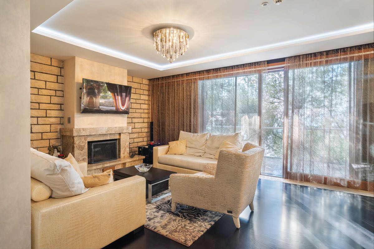 Living room with a fireplace and soft seating in a villa in Budva, Montenegro: stylish interior with a panoramic window view.