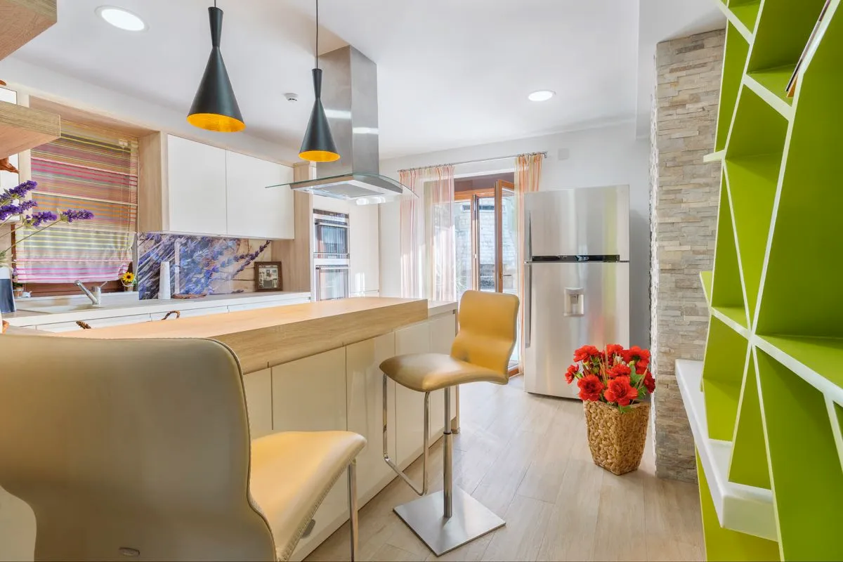 Modern kitchen featuring a wooden island, bar stools, stainless steel fridge, and pendant lights.