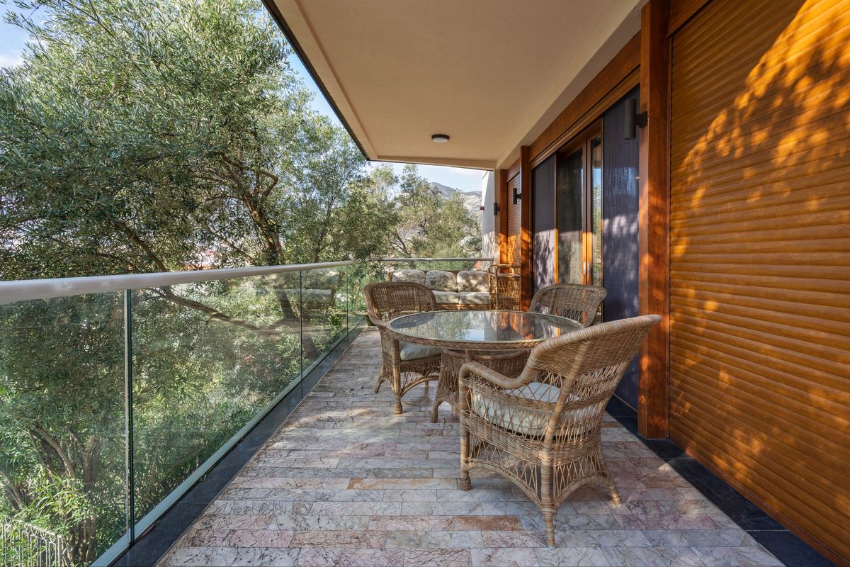 Cozy balcony with wicker furniture and a view of greenery at a villa in Budva, Montenegro: a terrace with a stone floor and railing.