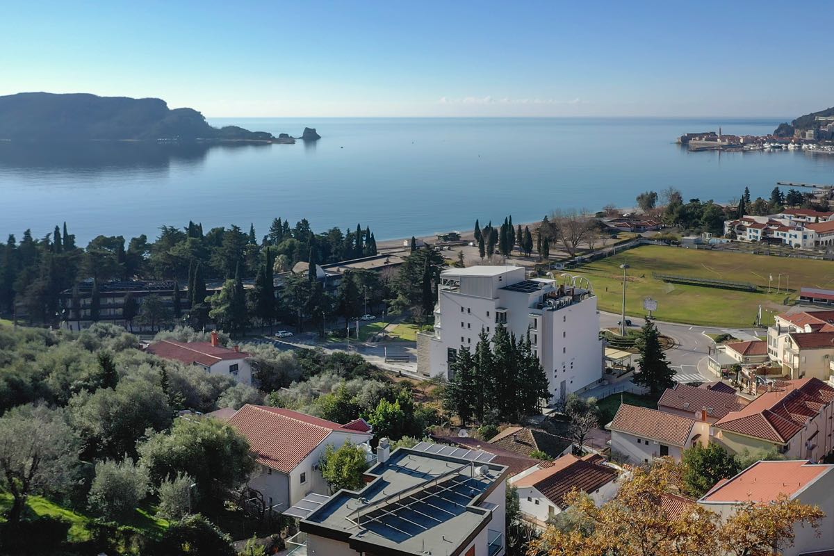 Panoramic view of the sea and the Budva coast, Montenegro: a modern villa, olive groves, and a beach in the distance.