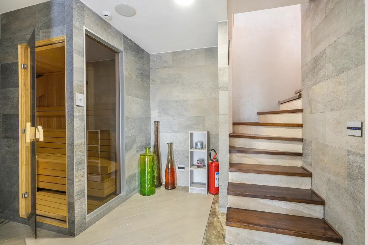 Hallway featuring a wooden sauna, glass door, stone walls, and a staircase with wooden steps and decorative vases.