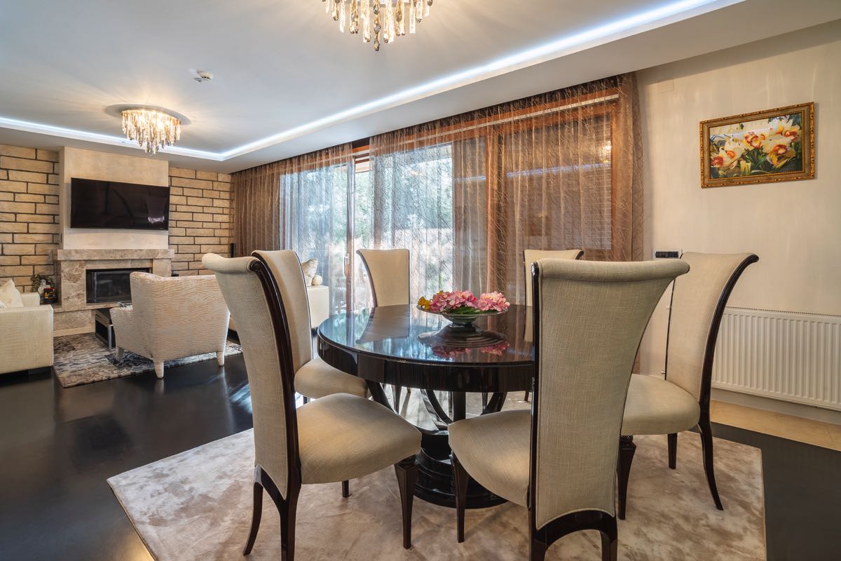 Living room with dining area and fireplace in a villa in Budva, Montenegro: modern interior, dark floor and chandeliers.