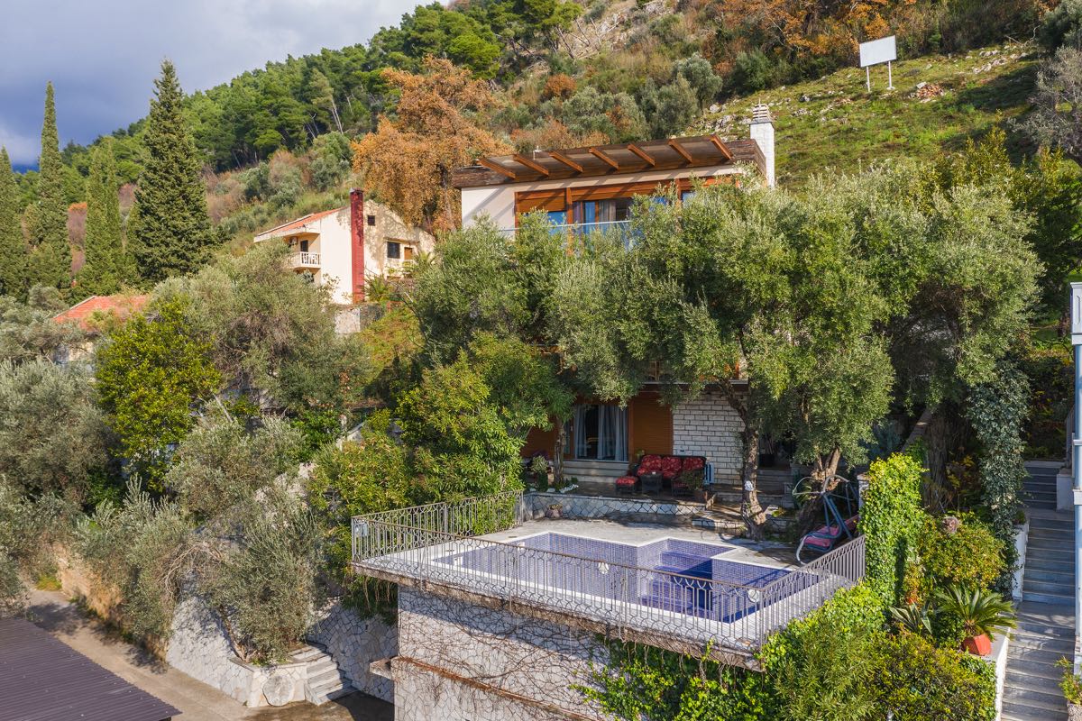 Two-story villa in Budva, Montenegro, with an outdoor pool, terrace, and garden on a mountainside among olive trees.