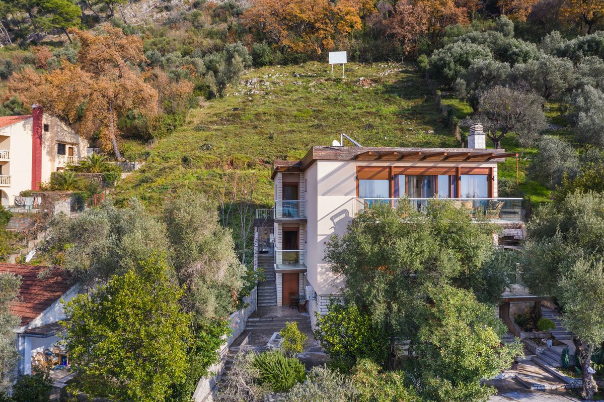 Three-story villa in Budva, Montenegro, with terraces, panoramic windows, and a green garden on a mountainside.