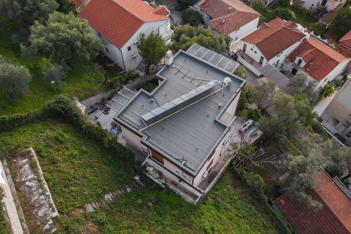 Aerial view of a villa in Budva, Montenegro: a flat roof with solar panels, a terrace, and a green plot around it.