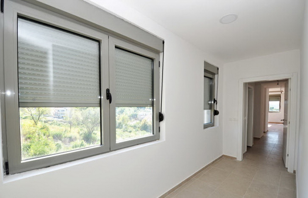 Bright room with windows and roller shutters in a new residential complex in Tivat, Montenegro, with a view of greenery and the corridor.