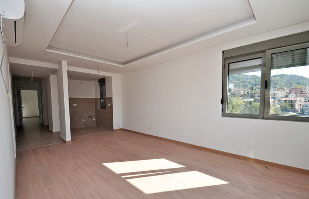 Bright living room with laminate flooring and a kitchen area in a new residential complex in Tivat, Montenegro, mountain view from the window.