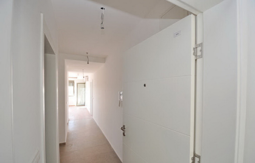 Bright hallway in a new apartment in a residential complex in Tivat, Montenegro: white walls, entrance door, and tiled floor.