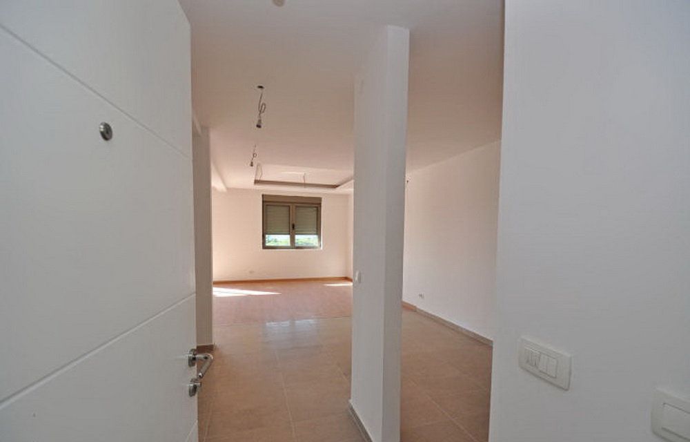 Bright living room in a new building in Tivat, Montenegro: white walls, tiled floor, and a window with blinds in an empty apartment.