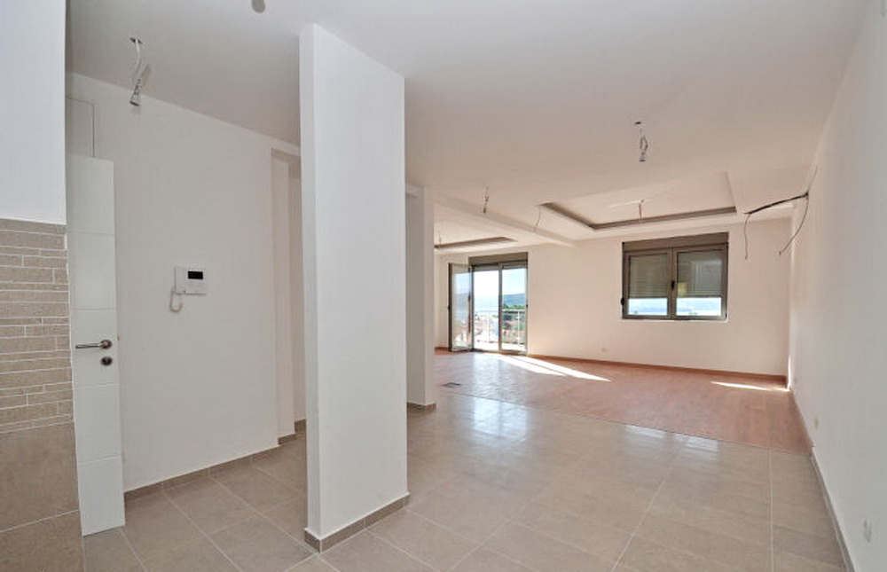 Spacious living room with finishes in a new building in Tivat, Montenegro: light walls, tiled floor, and sea view.