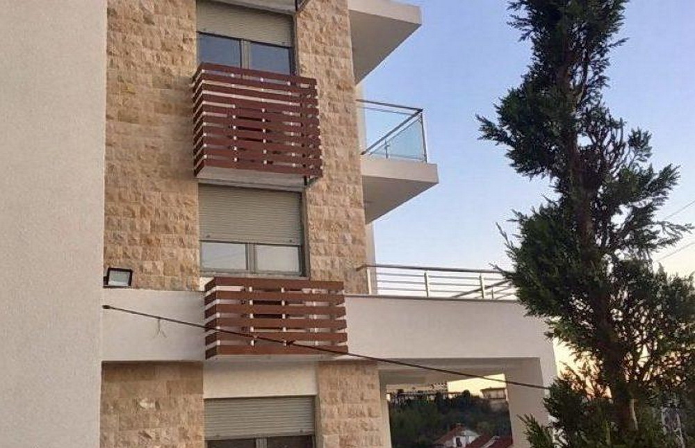 Facade of a modern residential complex in Tivat, Montenegro: stone cladding, balconies with wooden accents, and roller shutters.