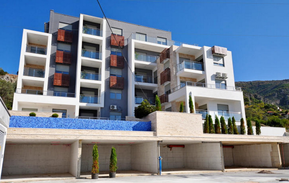 Modern residential complex in Tivat, Montenegro: facade with balconies, stone finish, and a swimming pool on the grounds.