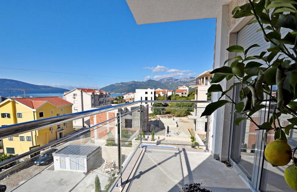 View from the balcony of a residential complex in Tivat, Montenegro: a panorama of mountains, sea, and modern buildings from the terrace.