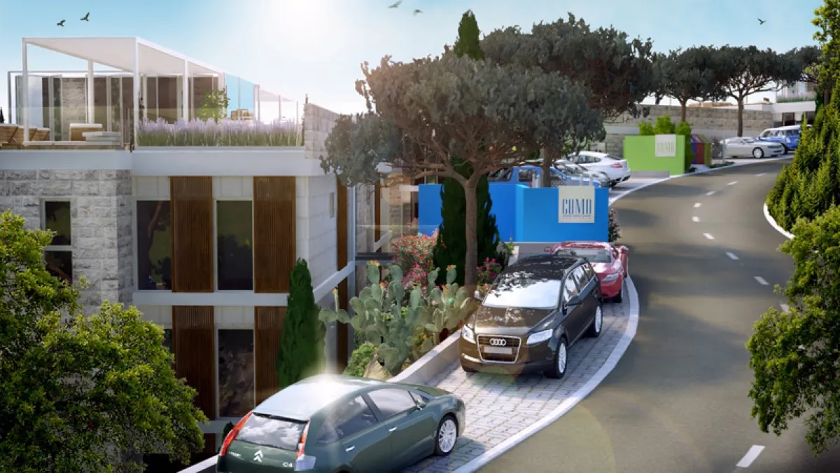 Exterior view of a modern building with parked cars, landscaping, and a paved driveway under sunlight.