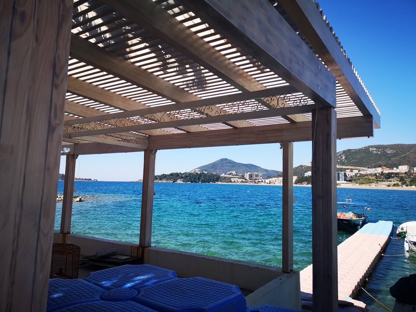 Terrace of a commercial space with a sea and pier view in Rafailovici, Montenegro, under a wooden canopy.