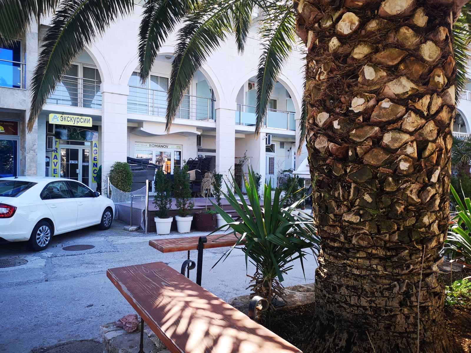 Facade of a commercial space in Rafailovici, Montenegro: entrance with arches, a palm tree, and parking by the restaurant.