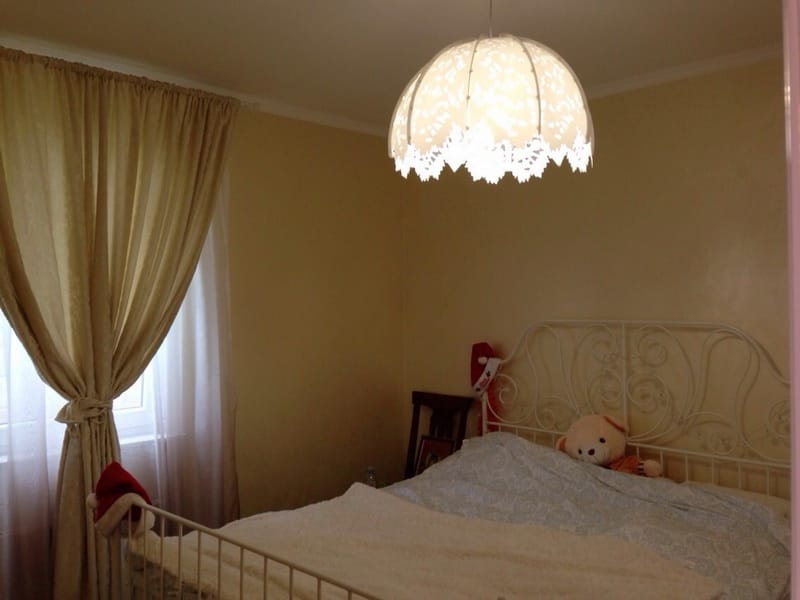 Cozy bedroom with a wrought-iron bed and an ornate light fixture in a villa in Shushan, Montenegro. Light tones, classic style.
