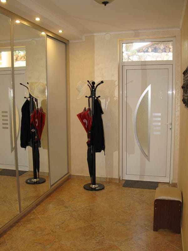 Villa hallway in Shushan, Montenegro: mirrored sliding wardrobe, freestanding coat rack, light finishes, and tiled floor.