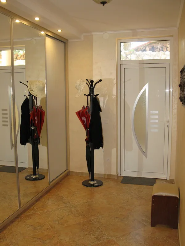Entryway featuring a main door, coat rack with umbrellas, large mirrored wardrobe, and tiled stone flooring.