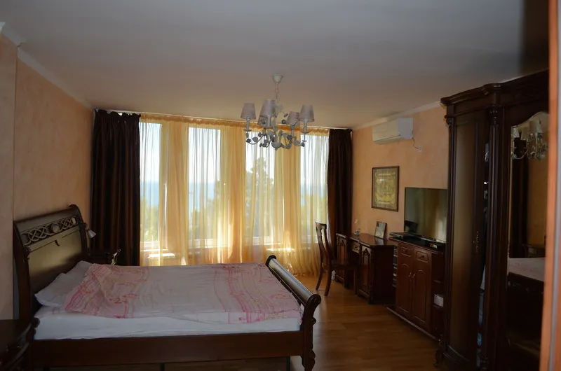 Bedroom featuring a wooden bed, wardrobe, TV, and large window with curtains.