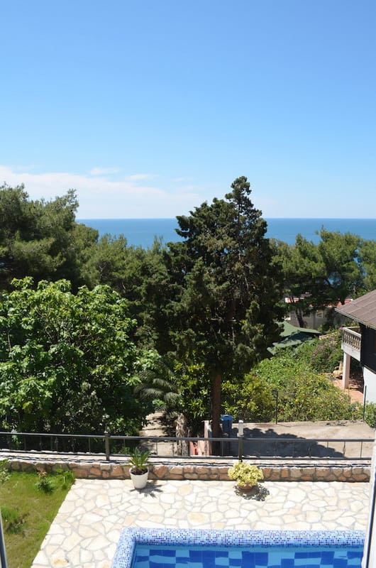 Sea and garden view from the terrace of a villa with a pool in Šušanj, Montenegro: stone finishes, conifer trees, and blue sky.