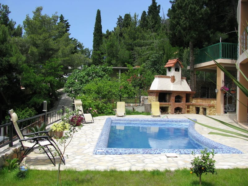 Pool with lounge and barbecue area at a villa in Shushan, Montenegro: stone terrace, sun loungers, and a garden with conifer trees.