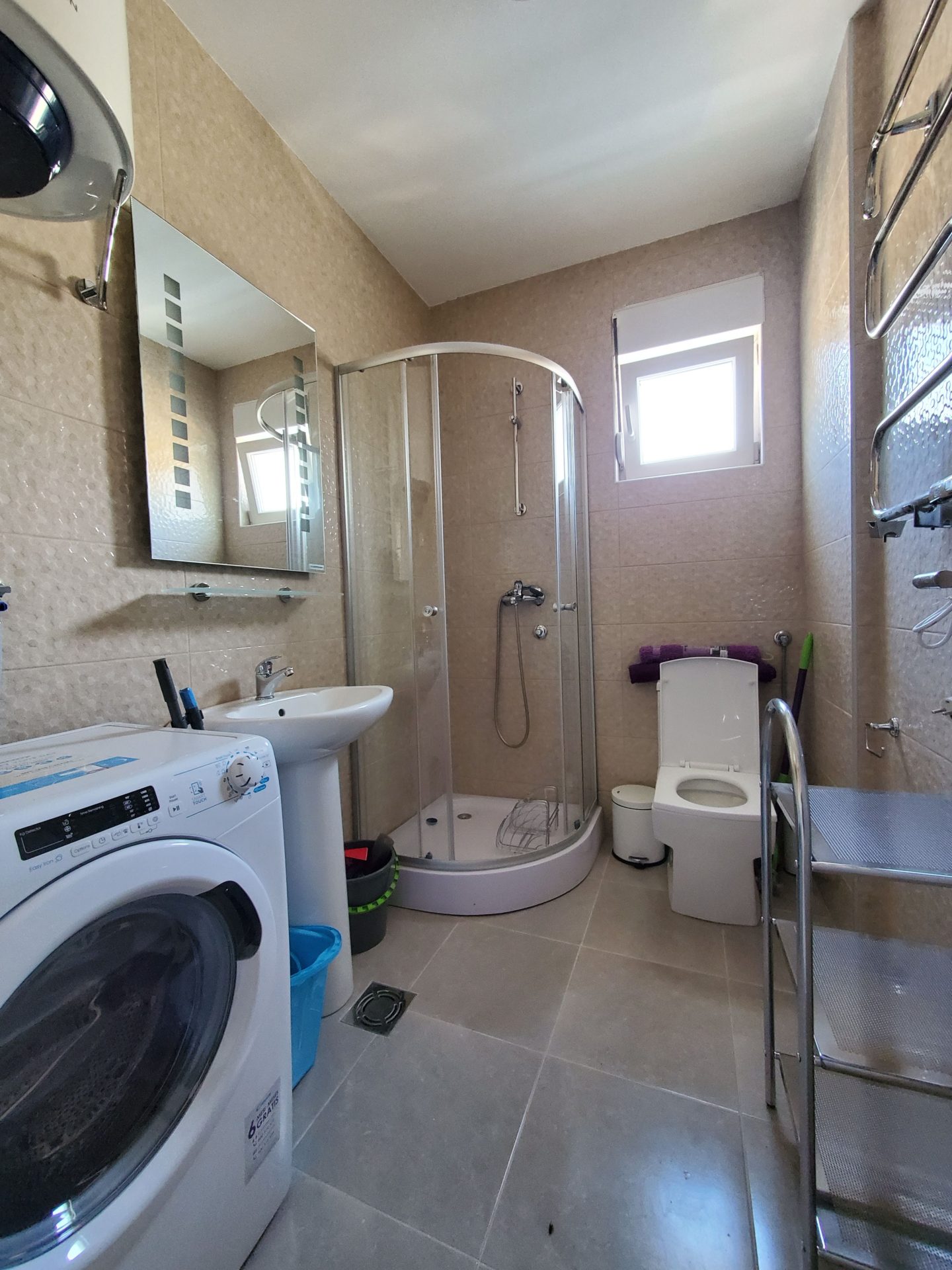 Bathroom in an apartment in Budva, Montenegro: shower cabin, washing machine, sink, and light-colored tiles.