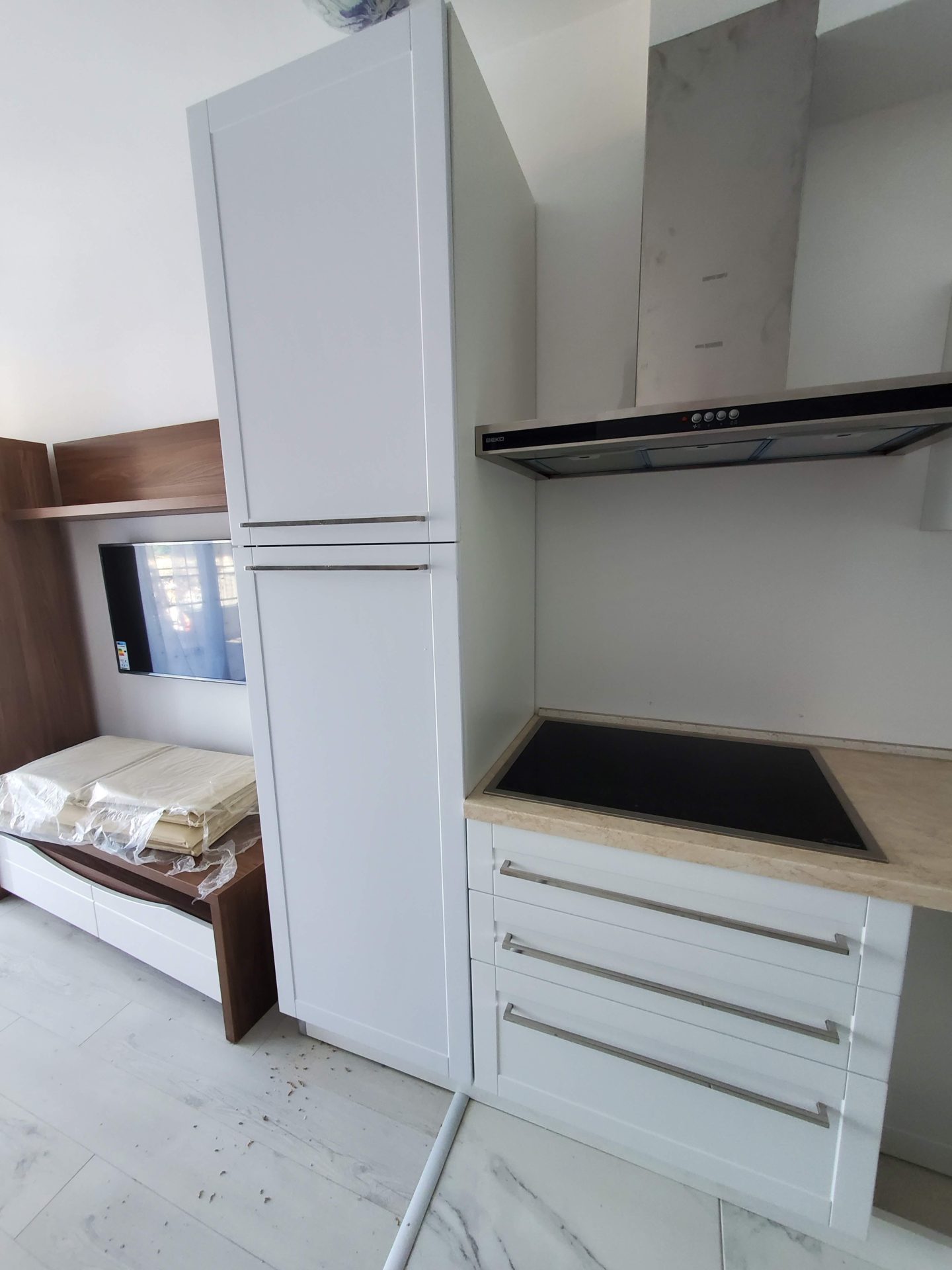Modern kitchen in an apartment in Budva, Montenegro: white fronts, built-in appliances, and a TV area in a bright interior.