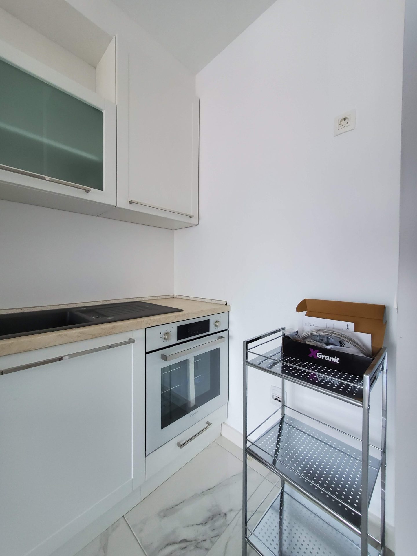 Modern white kitchen with appliances in an apartment in Budva, Montenegro: built-in oven and stone sink.