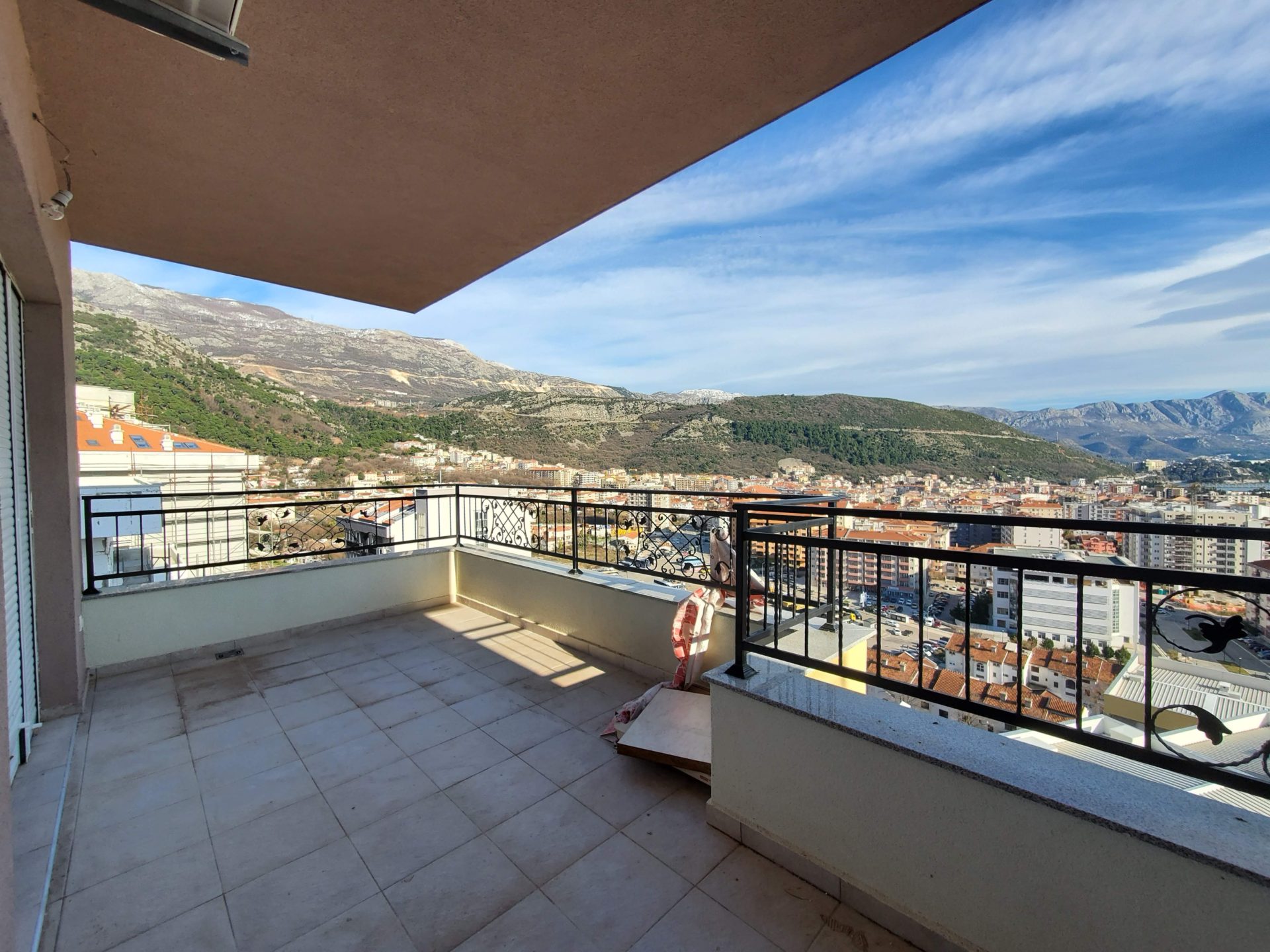 Spacious balcony with panoramic views of the mountains and the city of Budva, Montenegro, tiled flooring, wrought-iron railing.