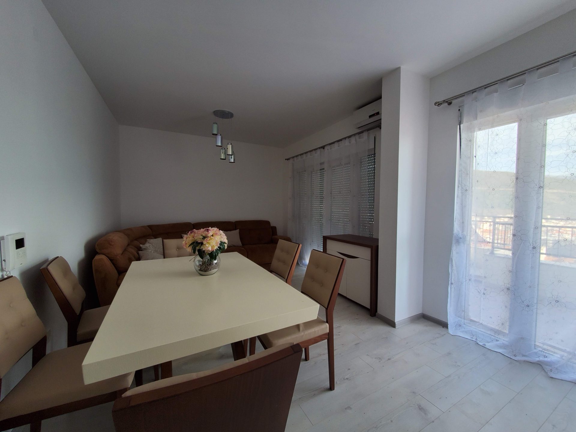 Bright living room with a dining area and a soft sofa in an apartment in Budva, Montenegro. Modern interior with access to the balcony.
