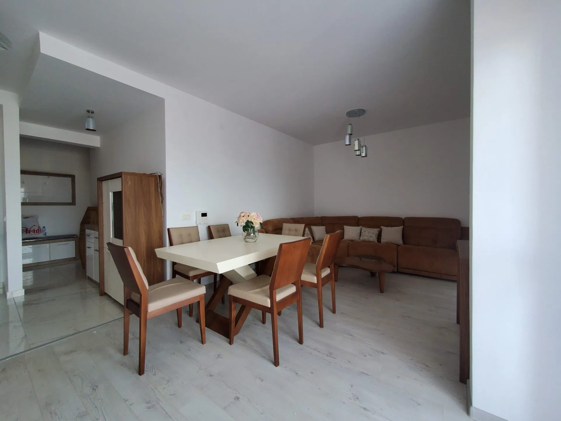 Living room featuring a brown sectional sofa and white dining table on light flooring.