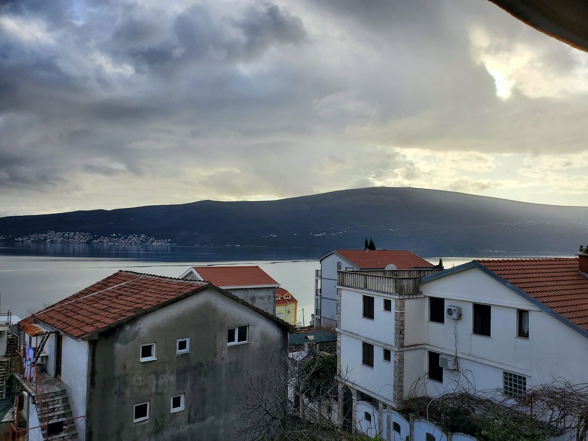 Sea and mountain view from a hotel in Bijela, Montenegro: a panorama of the coastline with residential buildings and tiled roofs.