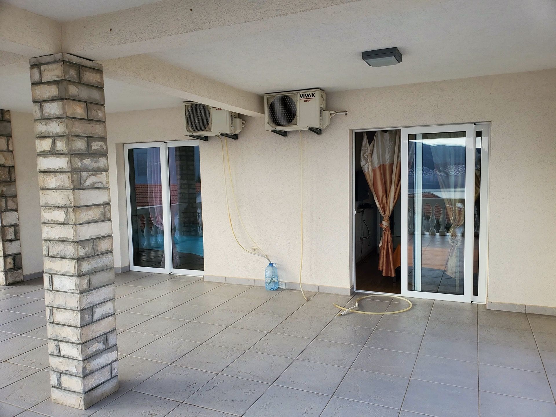 Spacious hotel terrace in Bijela, Montenegro, with a stone column, tiled floor, and access to the room through panoramic doors.