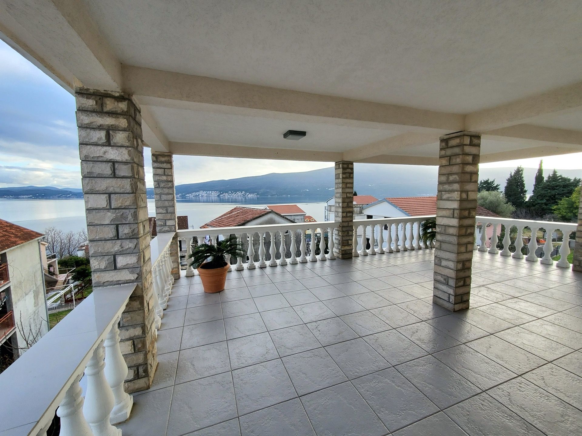Spacious hotel terrace in Bijela, Montenegro, with stone columns, balustrade, and panoramic sea and mountain views.