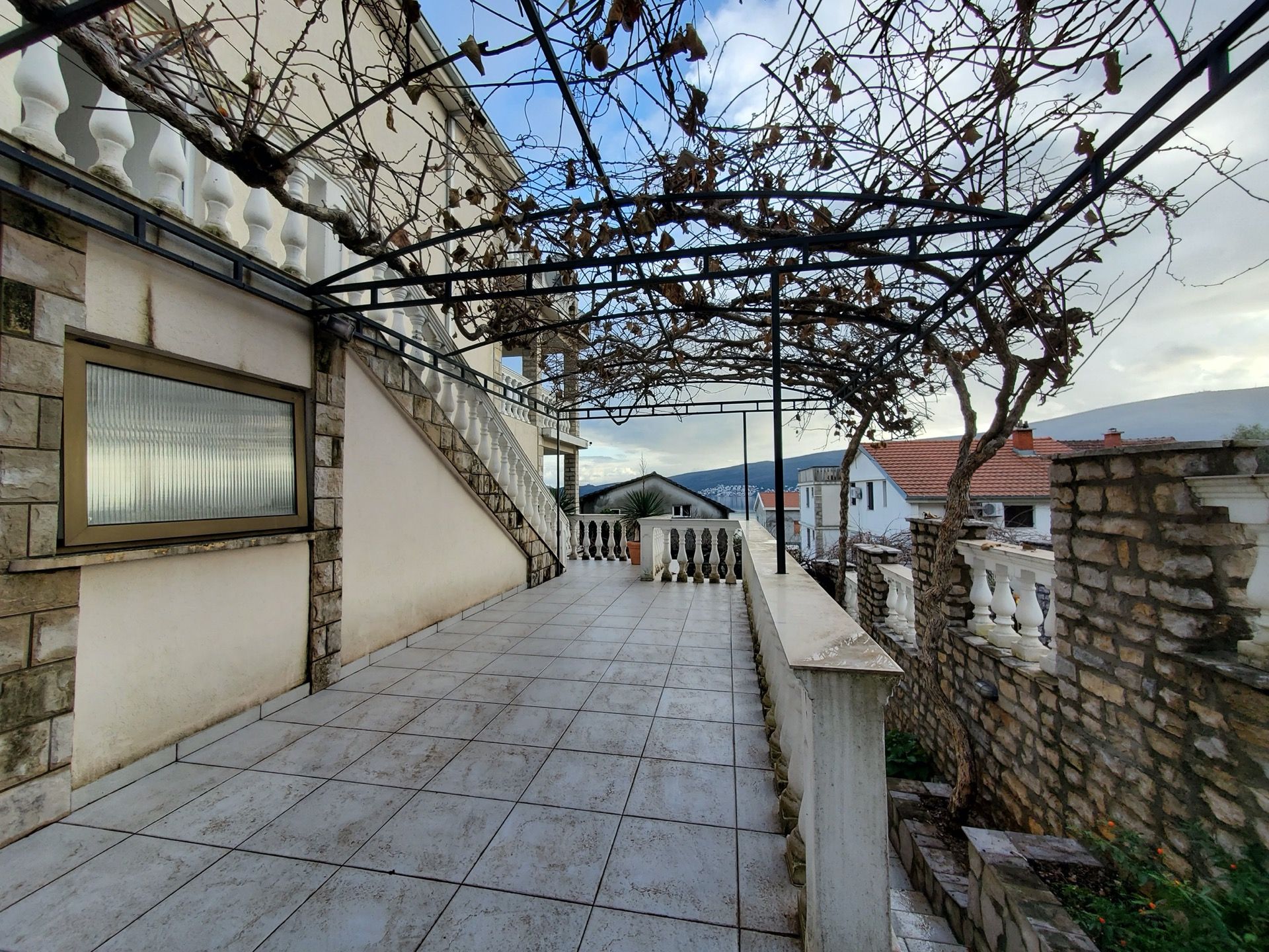 Hotel terrace in Bijela, Montenegro: balcony with stone finish, balustrade, and grapevine canopy.