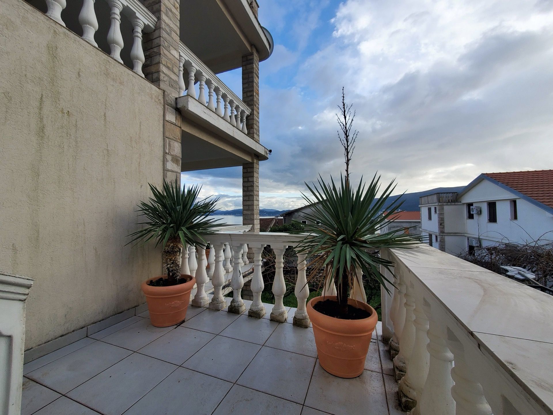Hotel balcony in Bijela, Montenegro: terrace with balustrade, potted plants, and panoramic sea view.