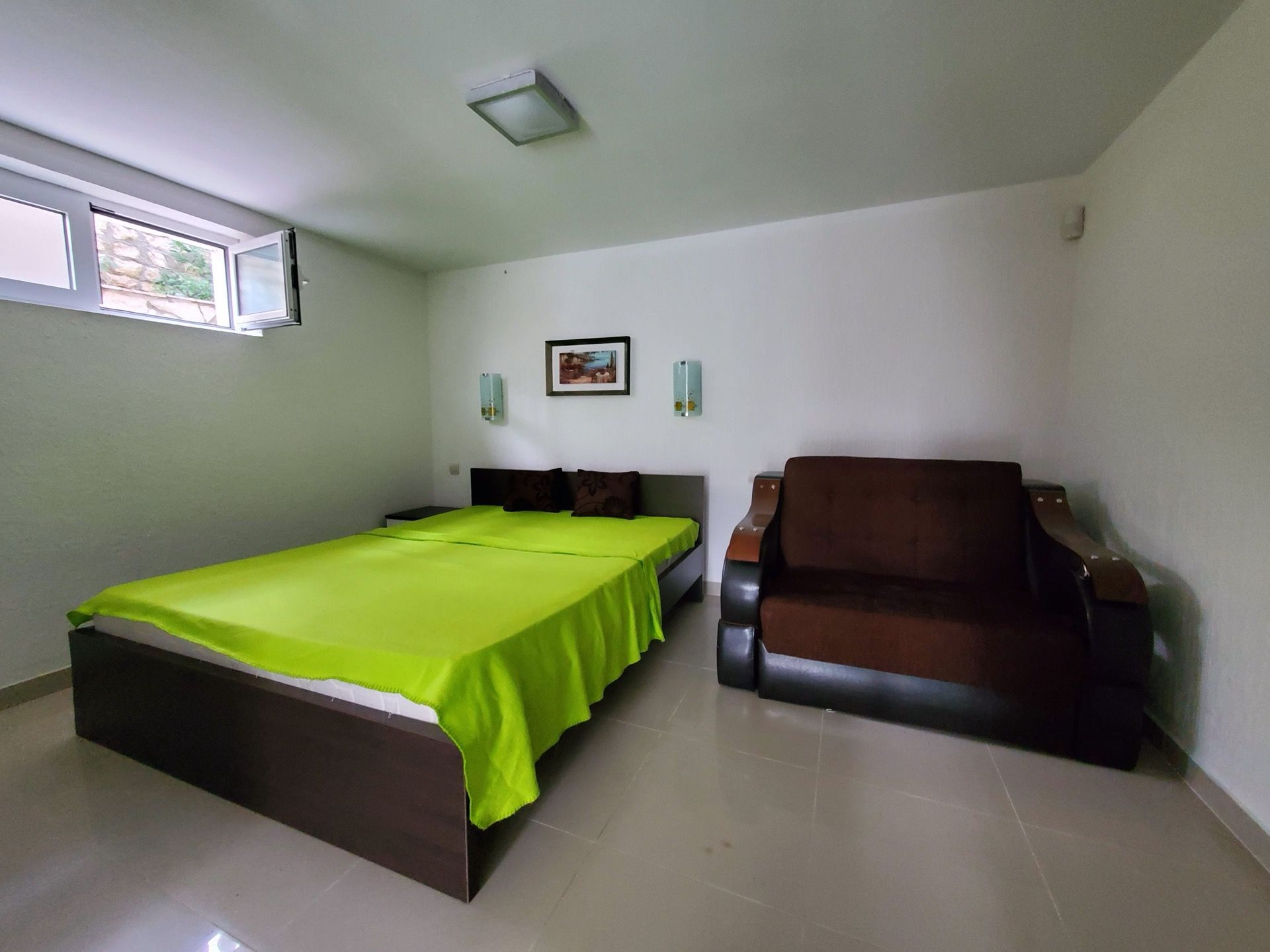 Bedroom in the Biela Hotel, Montenegro: a double bed with a bright bedspread, a brown sofa, and light finishes.