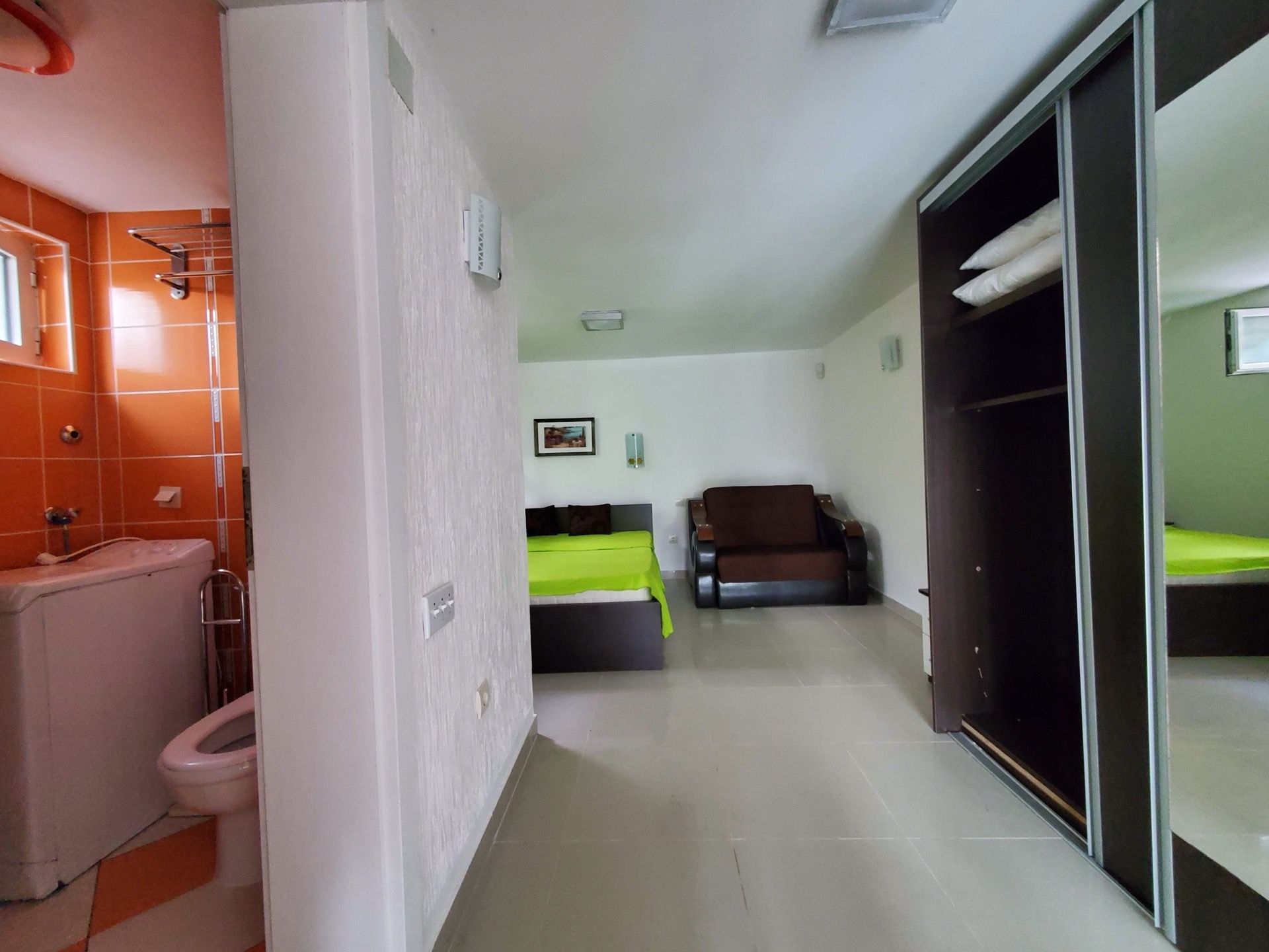 Hotel room interior in Bijela, Montenegro: bedroom with a bed, sofa, wardrobe, and a bathroom with orange tiles.