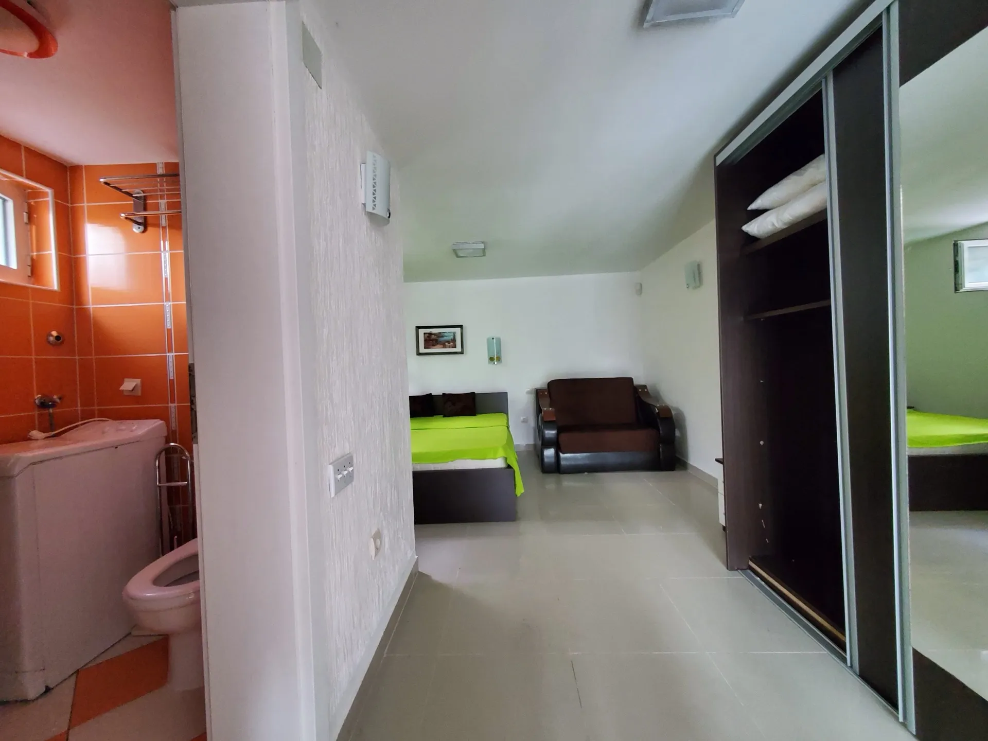 A bedroom with a bed and wardrobe is visible next to an attached bathroom containing a toilet and washing machine.