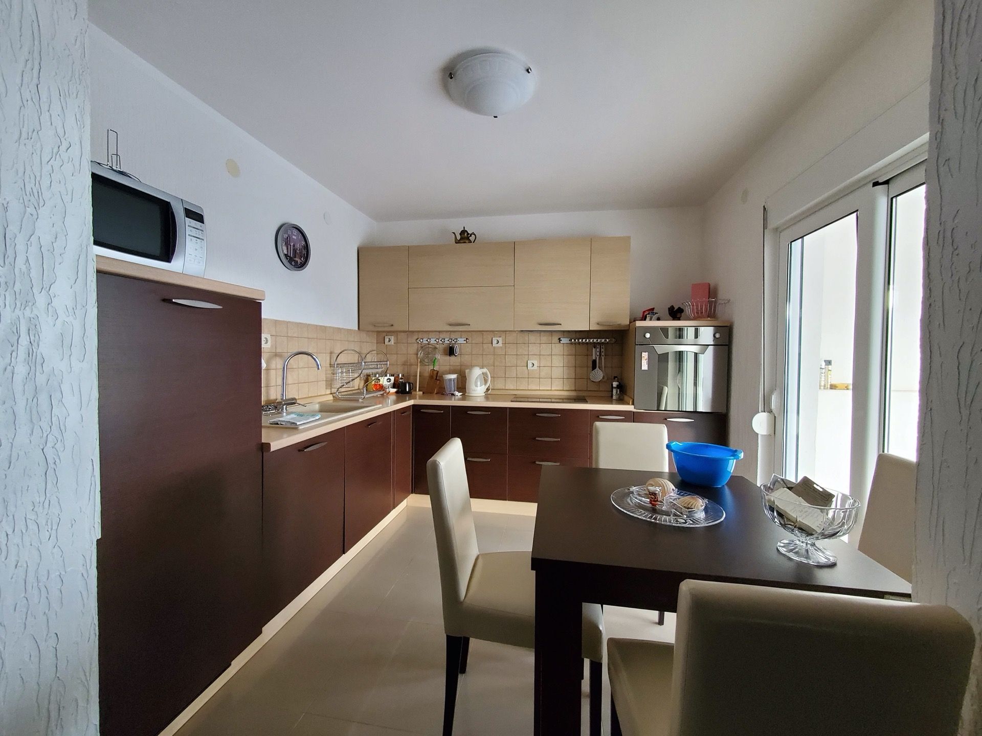 Modern kitchen with dining area in a hotel in Bijela, Montenegro: dark furniture, built-in appliances, and access to the balcony.