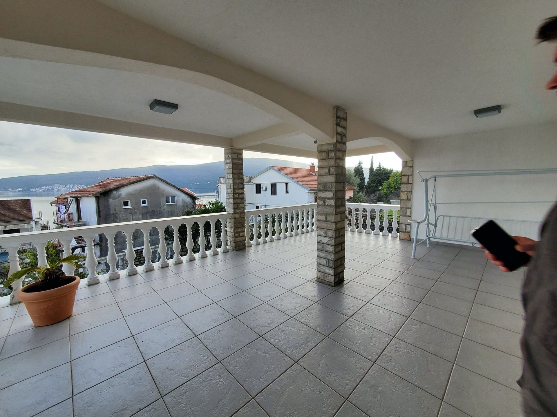 Spacious hotel terrace in Bijela, Montenegro, with tiled flooring, stone columns, and views of the sea and mountains.