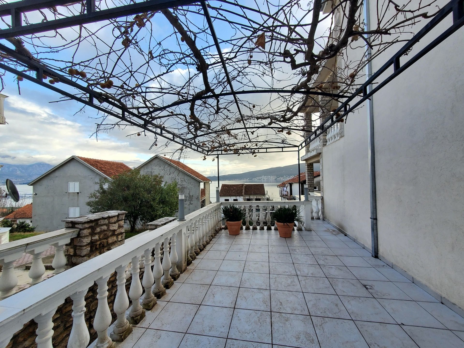 Spacious hotel terrace in Bijela, Montenegro, with a balustrade, grapevine canopy, and sea view.