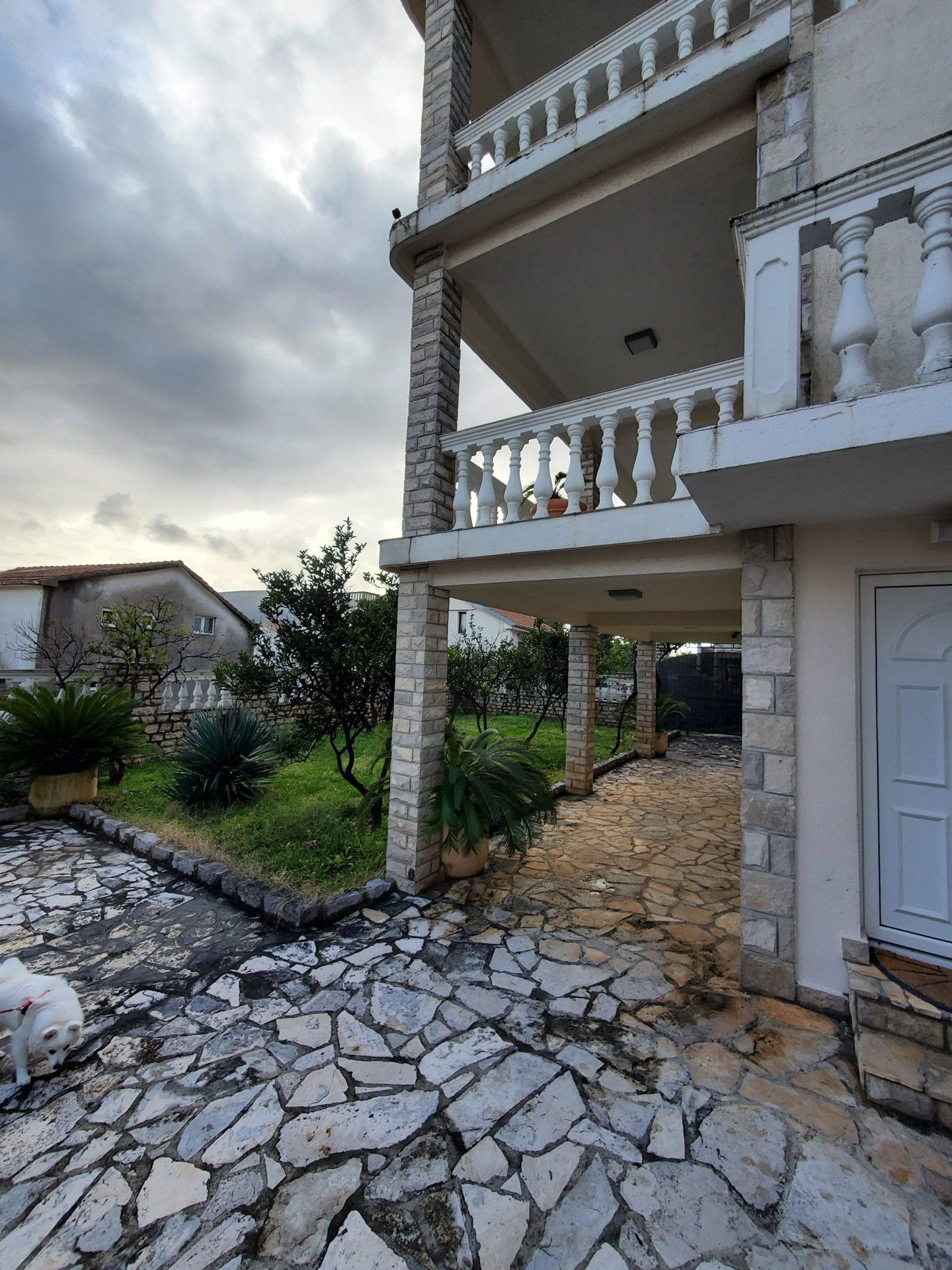 Two-story hotel in Bijela, Montenegro: stone facade finish, terraces with balustrades, and a green garden with pathways.